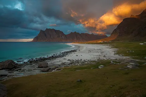 Uttakleiv 海滩的白沙、鹅卵石、草坡与山峰，云层映着夕阳