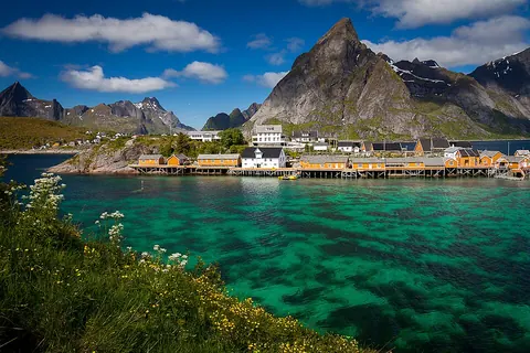 Sakrisøy 黄色渔屋沿海岸排列，前景是清澈的碧绿色海水
